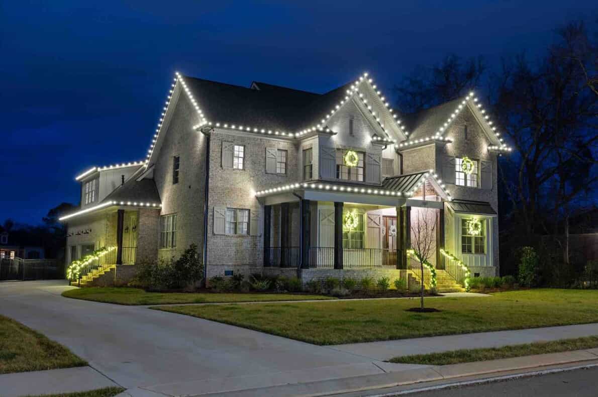 White Christmas lights on a home with a walkway and trees