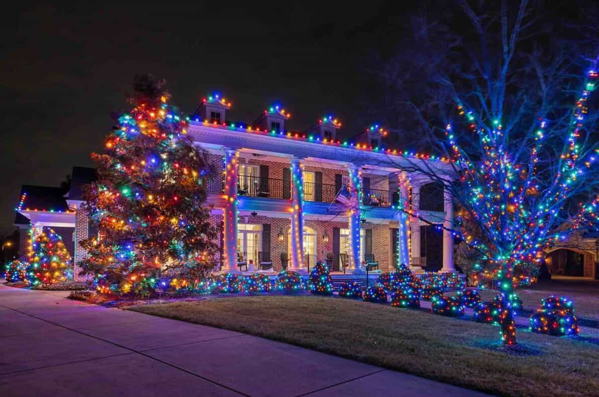 Multicolored Christmas lights on a home with a walkway and trees