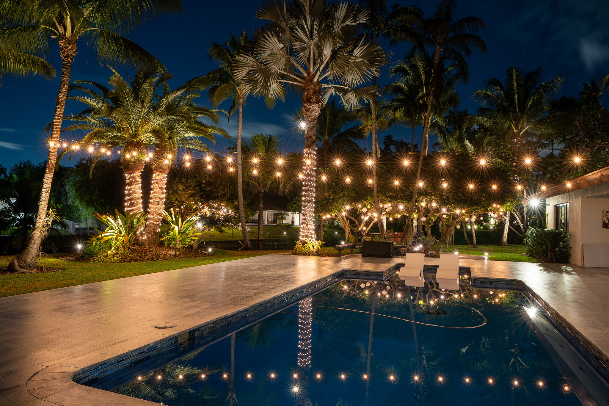 a pool with string lights overhead and light wrapped palm trees